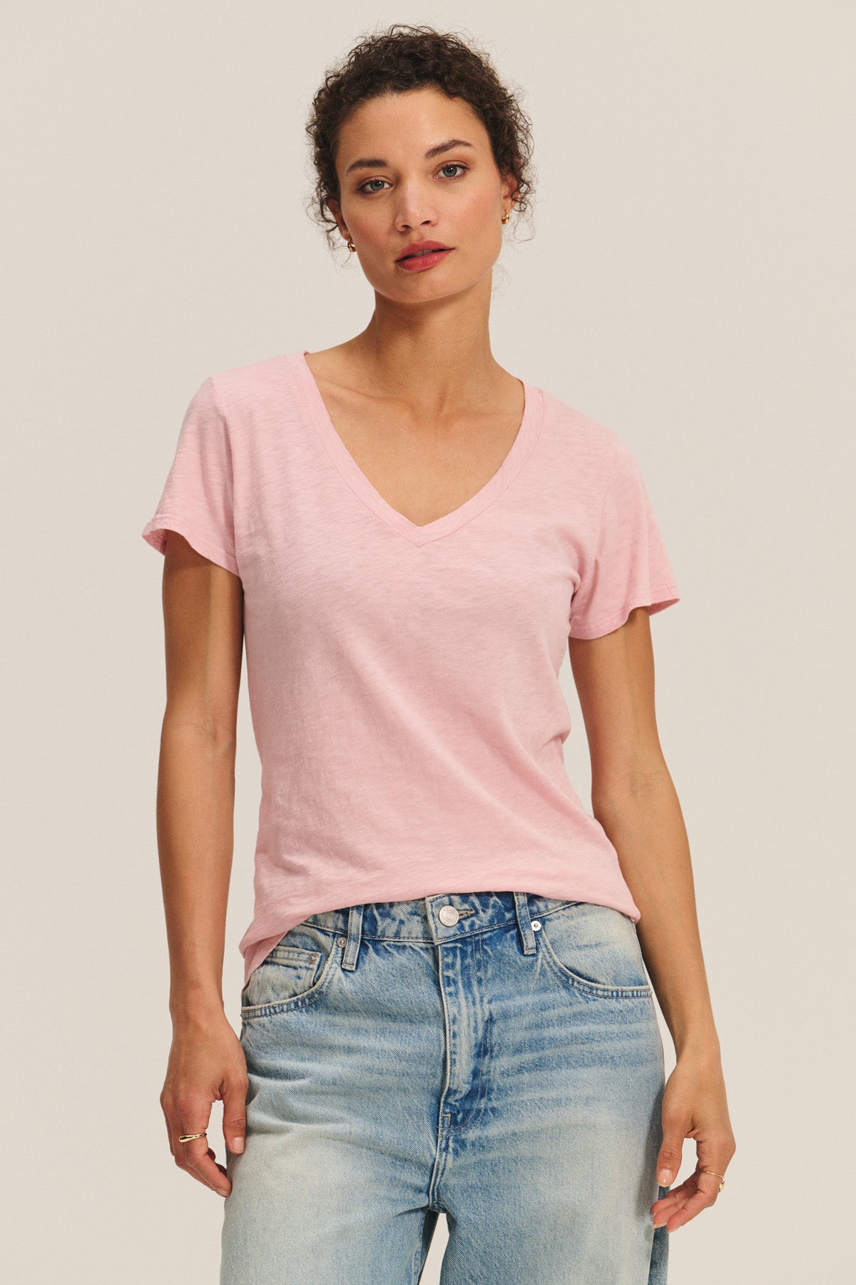 Someone wears the LILITH TEE by Velvet by Graham & Spencer in light pink with light blue jeans, standing against a plain light background.
