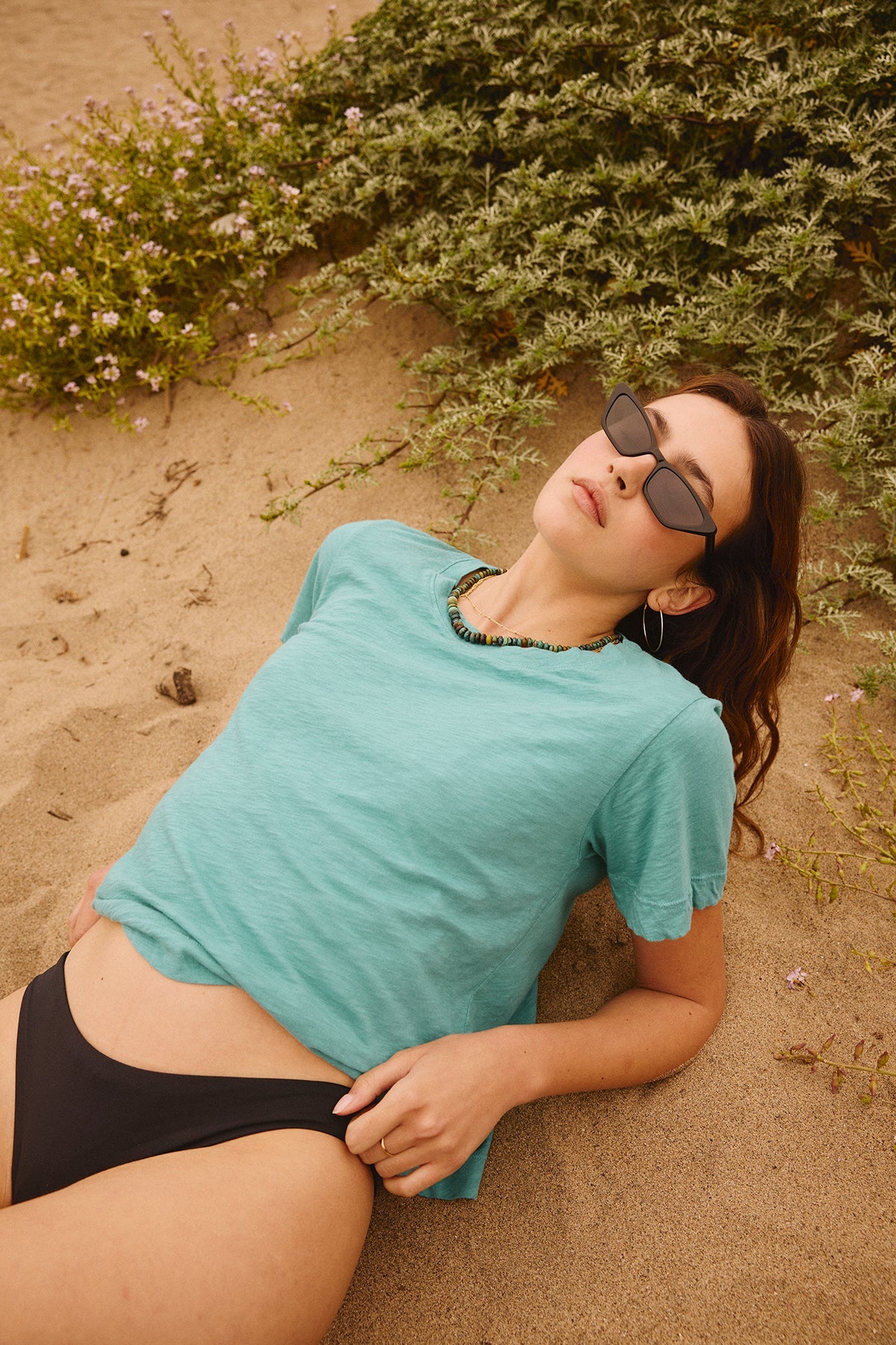 A woman in a black LULA COTTON SLUB SWING TEE by Velvet by Graham & Spencer laying on the sand.-35206647087297