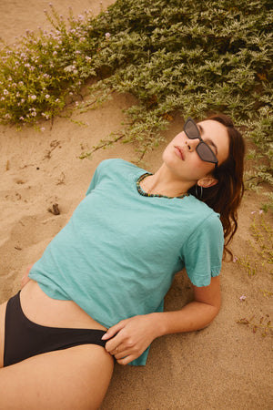 A woman in a black LULA COTTON SLUB SWING TEE by Velvet by Graham & Spencer laying on the sand.
