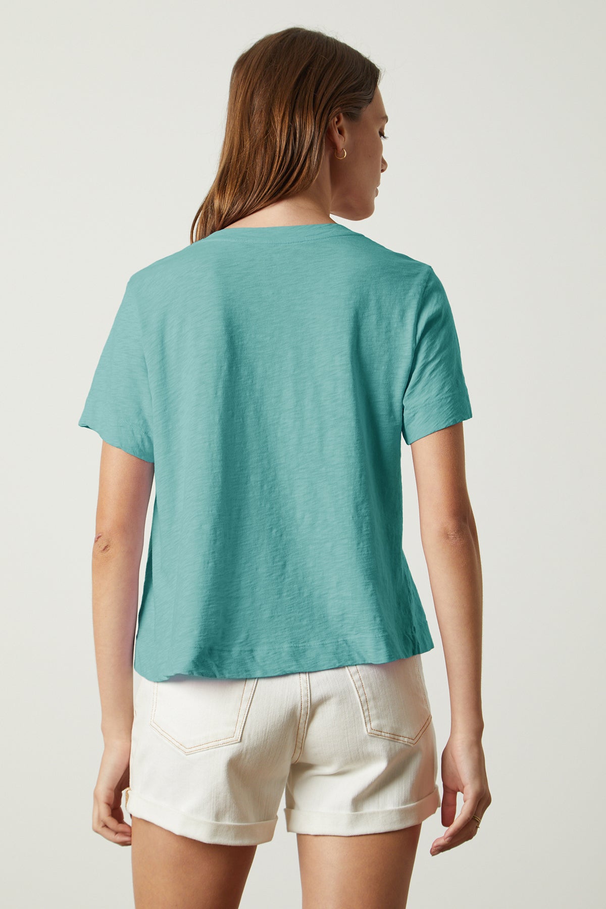   The back view of a woman wearing a Velvet by Graham & Spencer LULA COTTON SLUB SWING TEE and white shorts. 