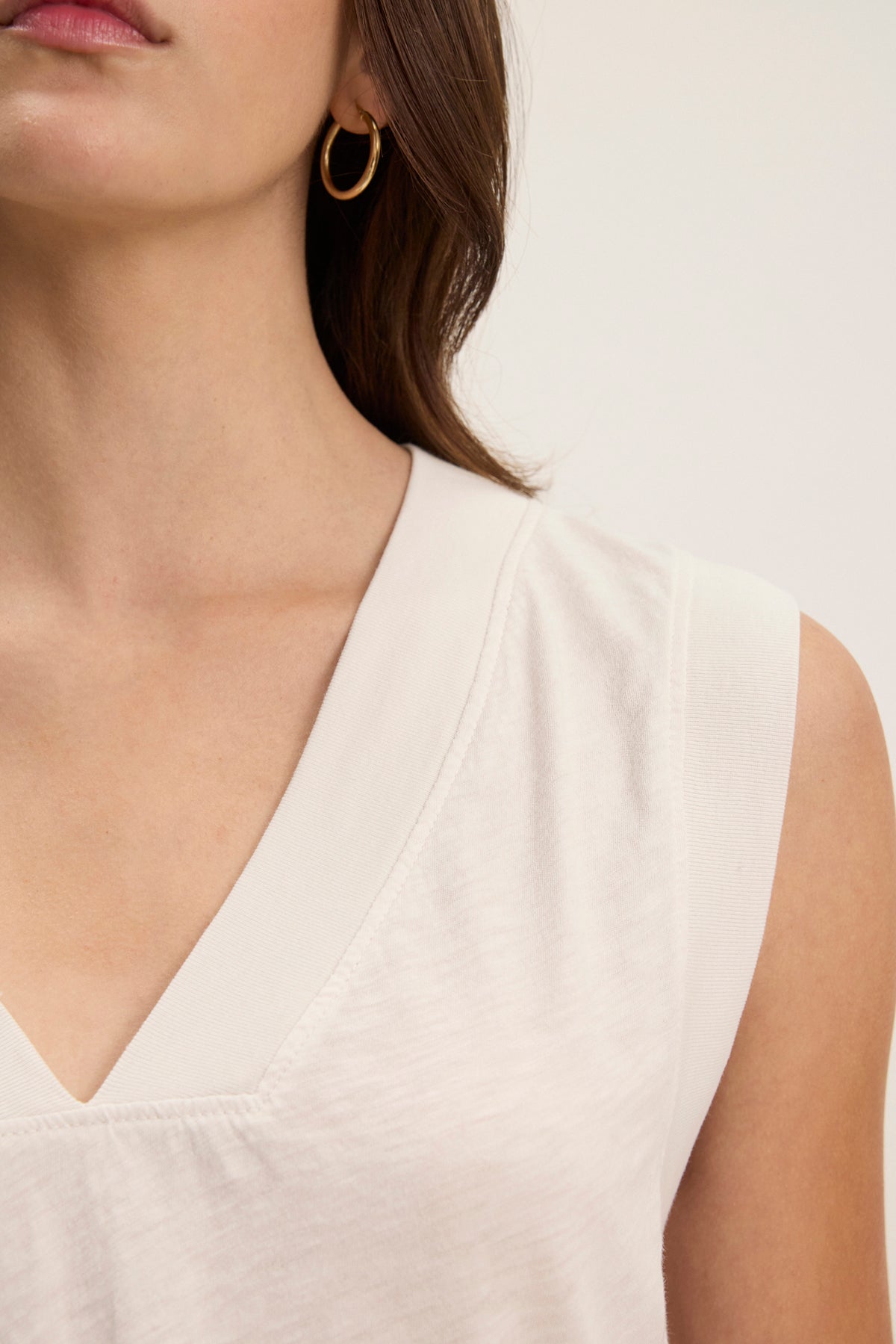 A woman wears the MARIA TEE by Velvet by Graham & Spencer—a white, textured cotton slub V-neck sleeveless top—with gold hoop earrings, shown from the shoulders up against a plain background.-Hover Image