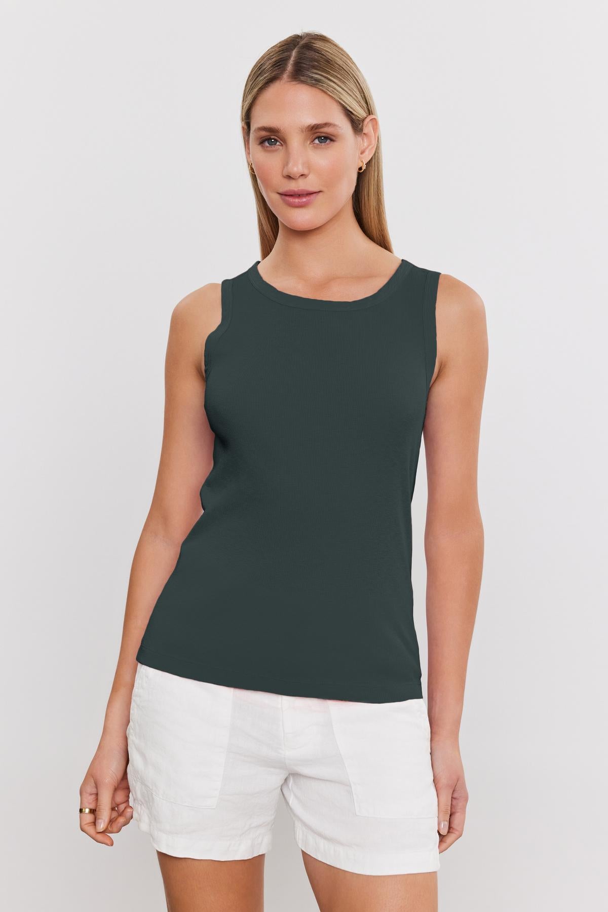 A person with long, blonde hair is wearing a sleeveless dark gray MAXIE RIBBED TANK TOP by Velvet by Graham & Spencer and white shorts, standing against a plain white background.-37241154437313