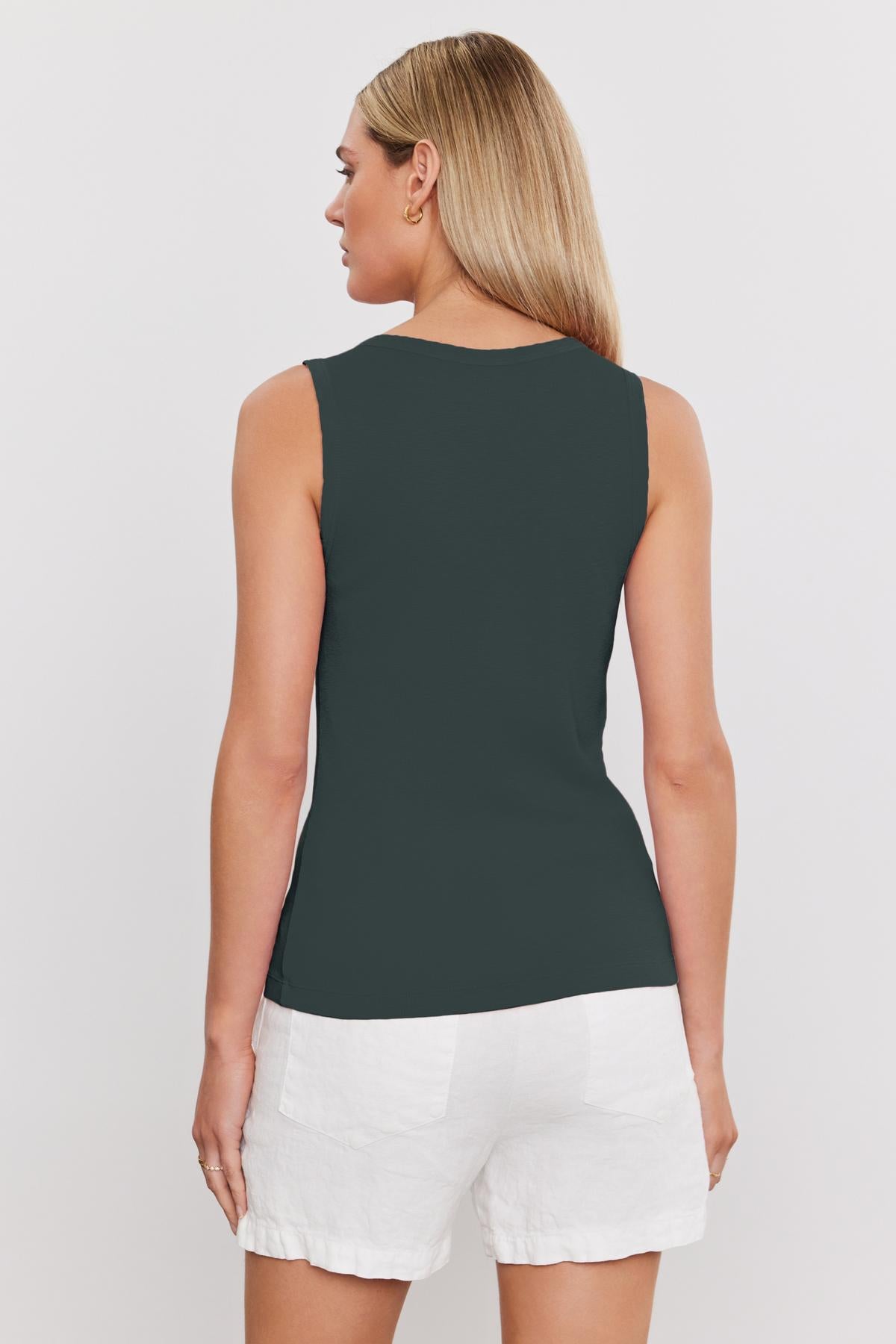 A person with long hair is seen from the back wearing a soft textured, sleeveless dark green MAXIE RIBBED TANK TOP by Velvet by Graham & Spencer and white shorts.-37241154502849