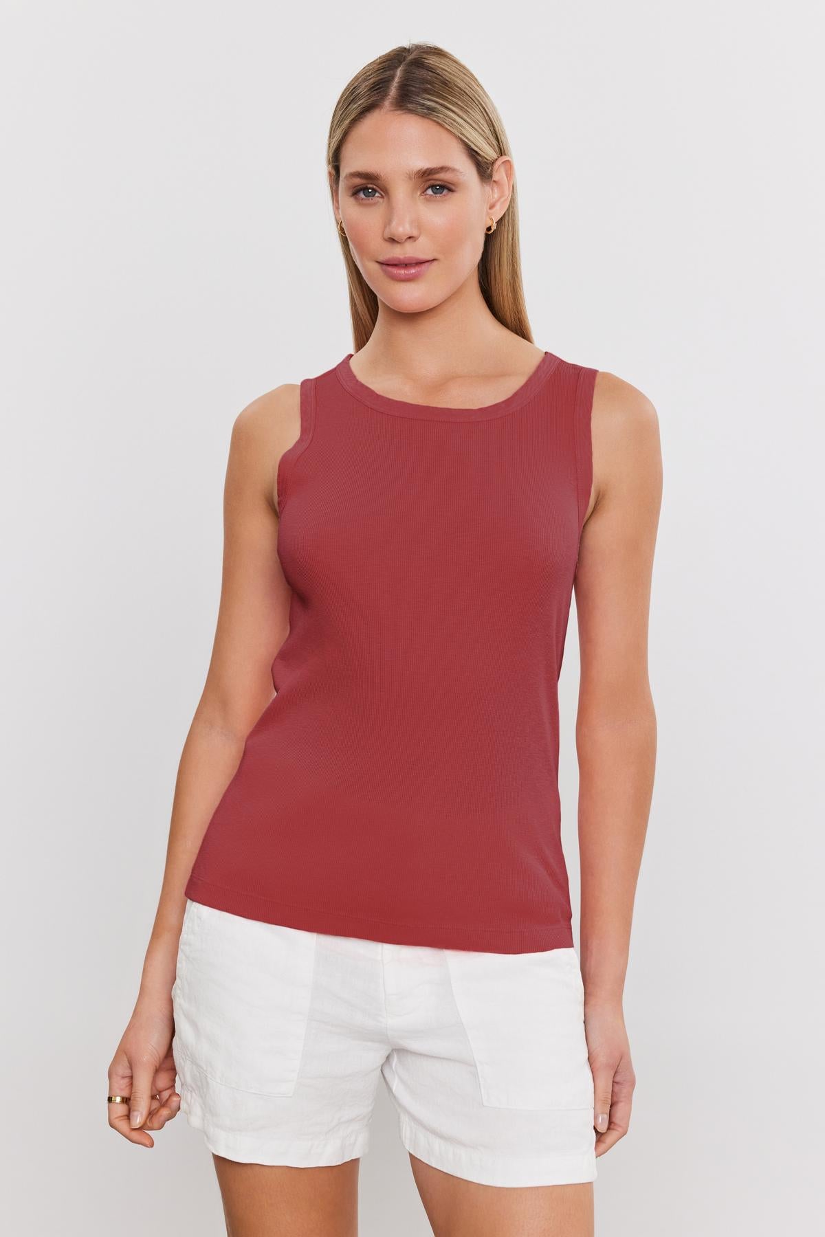 A woman with straight blonde hair is wearing a sleeveless red top and white shorts, standing against a plain white background. The soft-textured, slub knit fabric of her Velvet by Graham & Spencer MAXIE RIBBED TANK TOP adds a casual yet chic feel to her outfit.-37241154535617