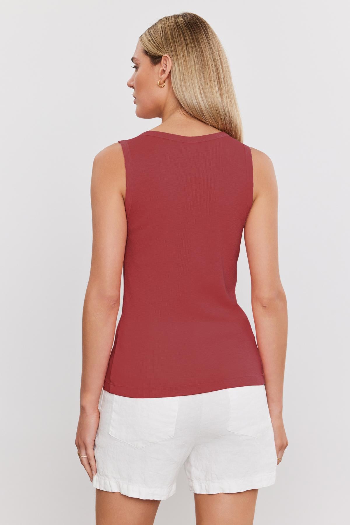   A woman with long blonde hair is seen from the back, wearing a sleeveless red MAXIE RIBBED TANK TOP by Velvet by Graham & Spencer and white shorts. 
