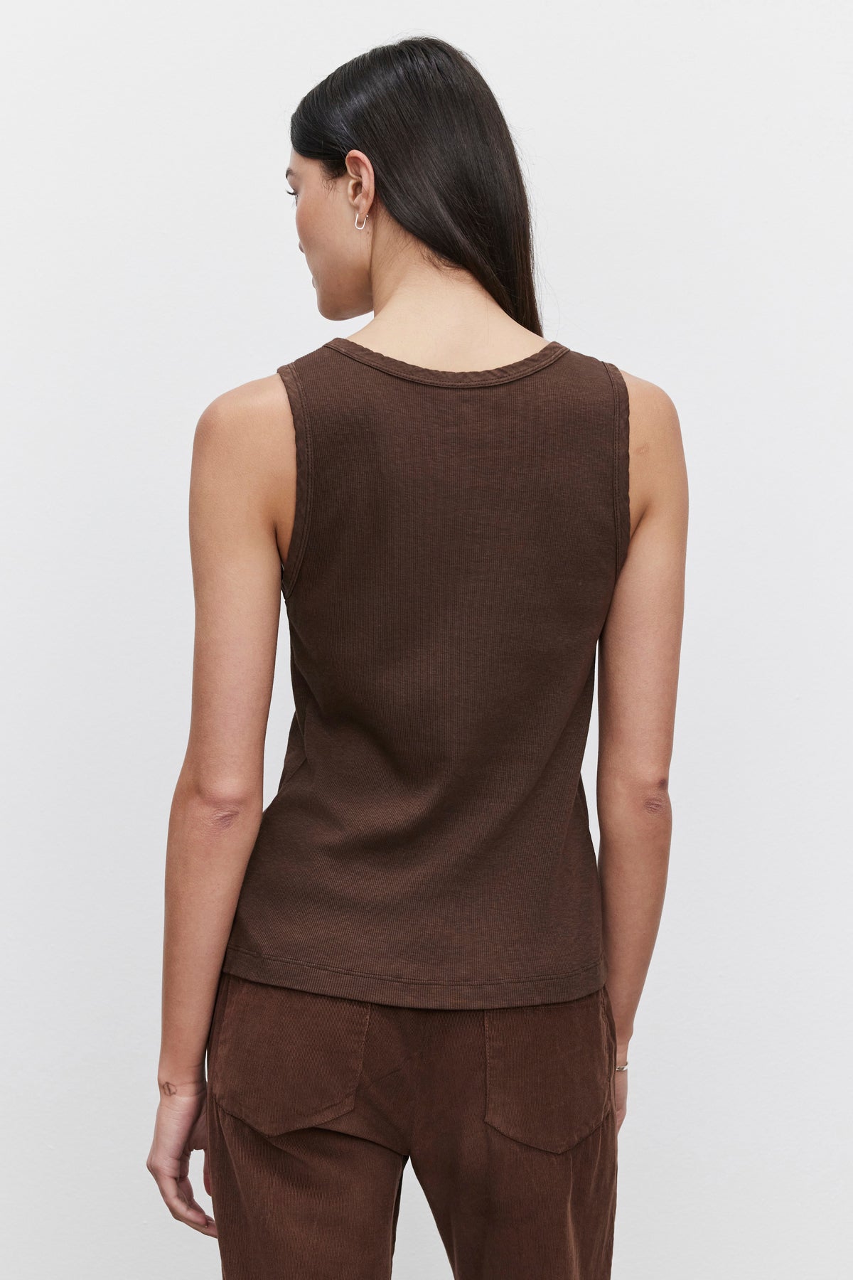   A person wearing the MAXIE RIBBED TANK TOP by Velvet by Graham & Spencer and brown pants is standing with their back to the camera against a plain white background, highlighting the slub knit fabric’s soft texture. 