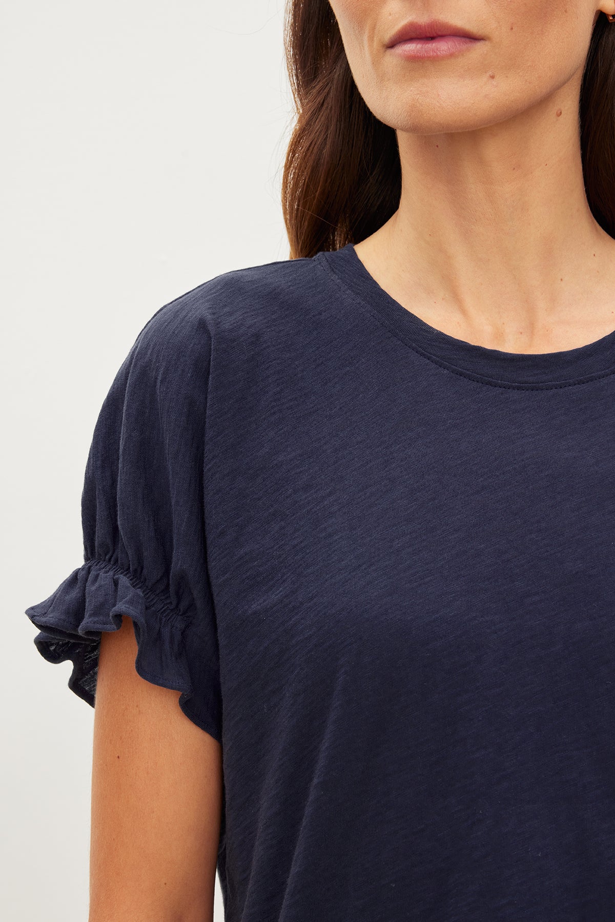   A woman wearing a navy cotton slub MIMI CREW NECK TEE with ruffle sleeves, an essential addition to her wardrobe with a crew neckline by Velvet by Graham & Spencer. 