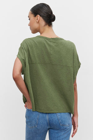 Woman from behind wearing a green Caroline Cocoon Top by Velvet by Graham & Spencer and blue jeans, standing with her left hand on her hip.