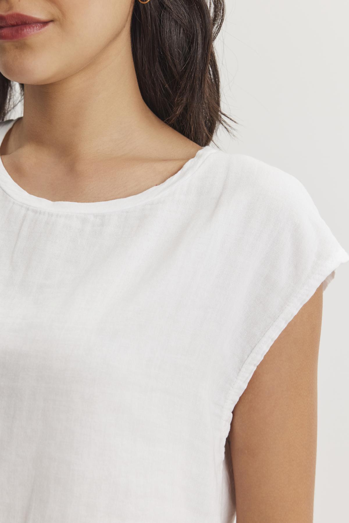   A close-up of a person wearing a white DANIELLA CREW NECK TEE from Velvet by Graham & Spencer made from lightweight cotton woven fabric. Only the lower half of their face and upper torso are visible, offering a casual basic look in a cropped silhouette. 
