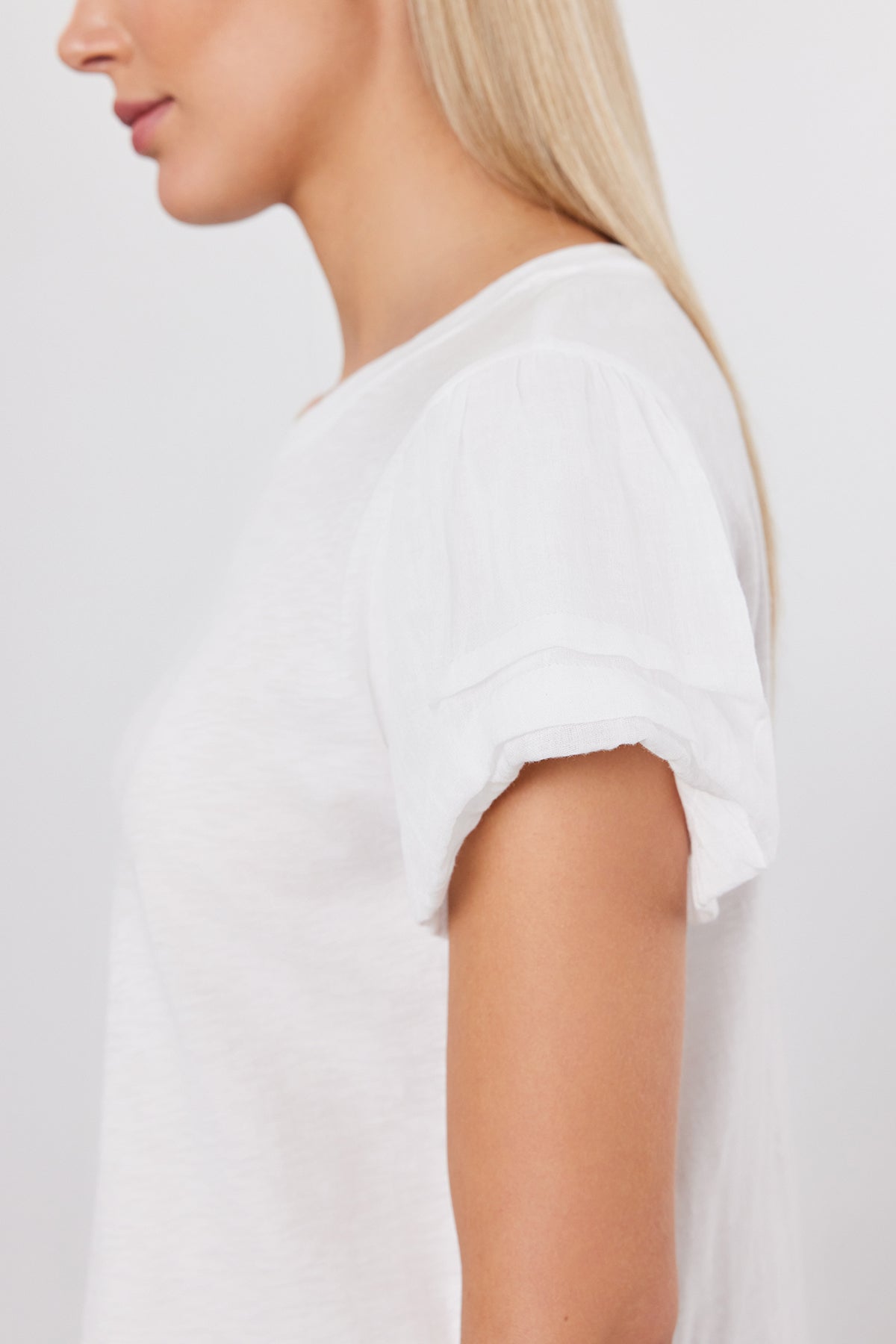   Side profile of a person with long blonde hair, wearing the Velvet by Graham & Spencer DELLA TEE, a white short-sleeved top with pleated sleeves. 