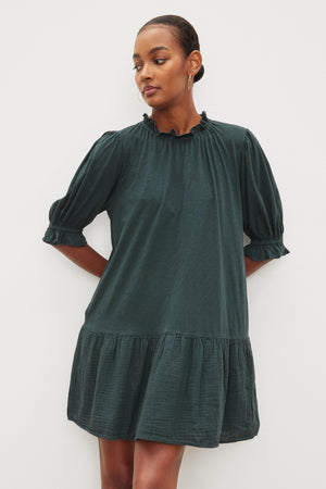 The model is wearing a Velvet by Graham & Spencer green Dillon tiered dress with ruffled sleeves.