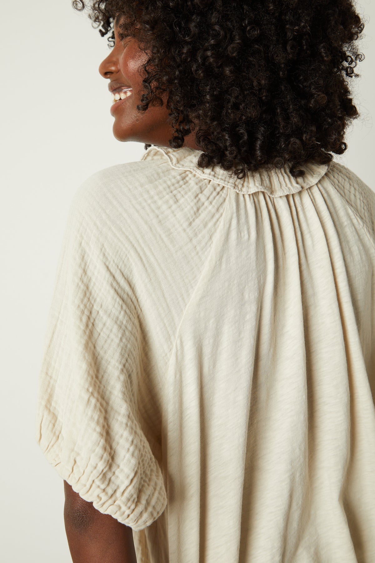   A woman wearing an Ilene puff sleeve top by Velvet by Graham & Spencer with a ruffle neck collar. 
