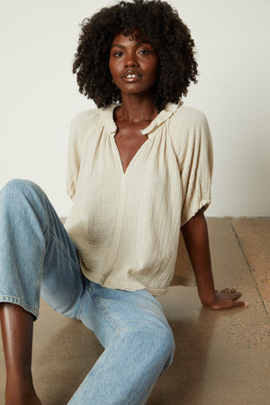 A black woman is sitting on the floor wearing jeans and a Velvet by Graham & Spencer Ilene Puff Sleeve Top.