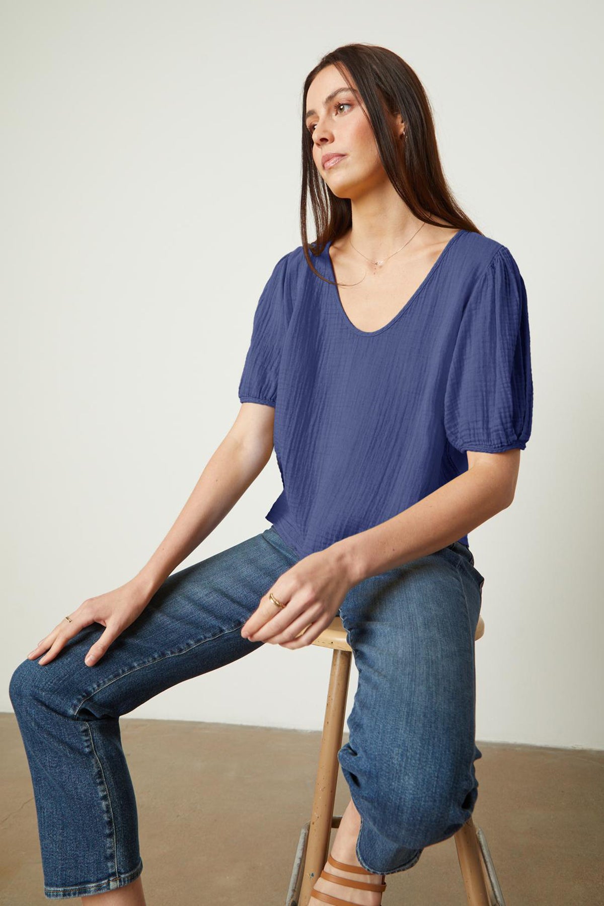  A woman is sitting on a stool wearing jeans and a Velvet by Graham & Spencer LOUISA PUFF SLEEVE TOP. 