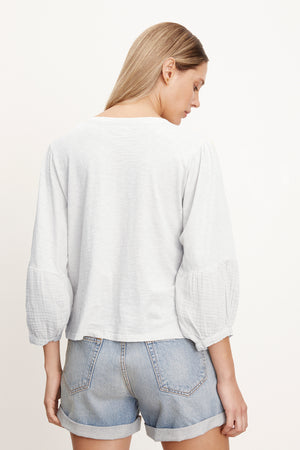 The back view of a woman wearing Velvet by Graham & Spencer denim shorts and a white MARIEL PUFF SLEEVE TEE.