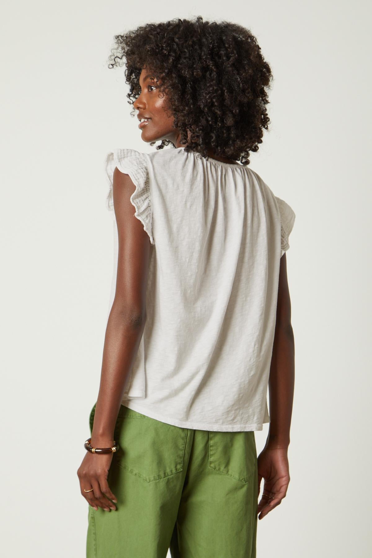 the back view of a woman wearing green pants and a Velvet by Graham & Spencer REMI RUFFLE SLEEVE TOP.-26572692947137