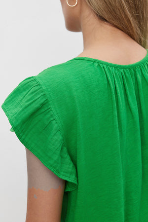 Person wearing a REMI RUFFLE SLEEVE TOP by Velvet by Graham & Spencer seen from the back, with shoulder-length hair and gold hoop earrings, exuding a subtle spring vibe.