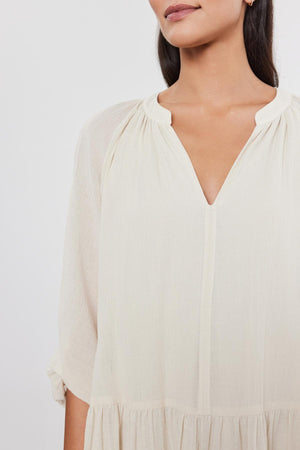 Woman in a white Velvet by Graham & Spencer Sloan Dress with a v-neckline and pleat detailing at the shoulders; only the top half of her body is visible.