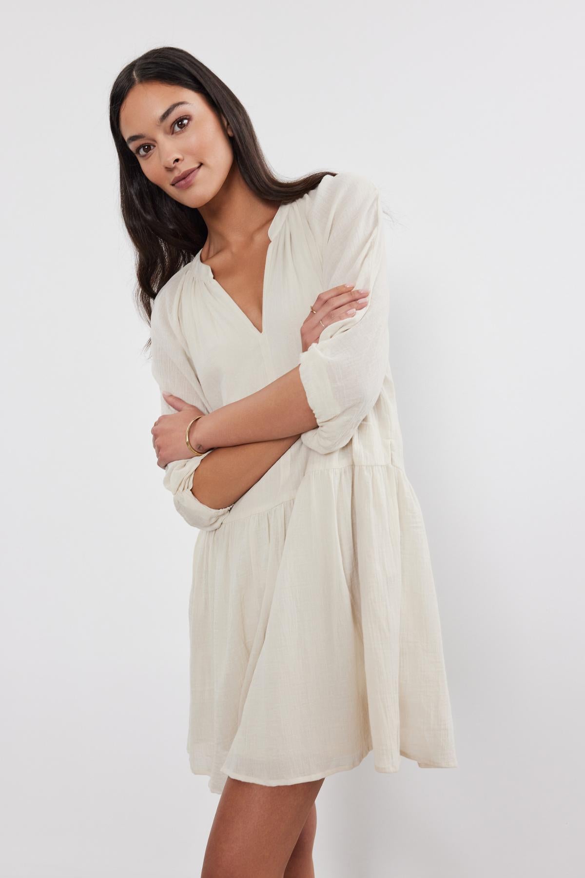   Woman in a cream Velvet by Graham & Spencer Sloan Dress posing with arms crossed, standing against a plain white background. 