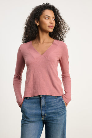 A woman wears the NESSA TEE by Velvet by Graham & Spencer with blue jeans, hands in her pockets, gazing to the side for a relaxed modern look against a plain background.