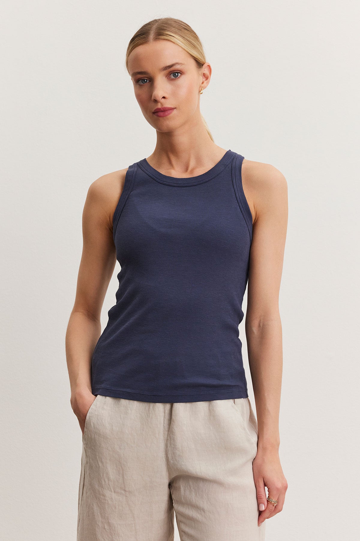   A woman in a navy blue Velvet by Graham & Spencer NOLA tank top and beige pants standing against a plain background. 