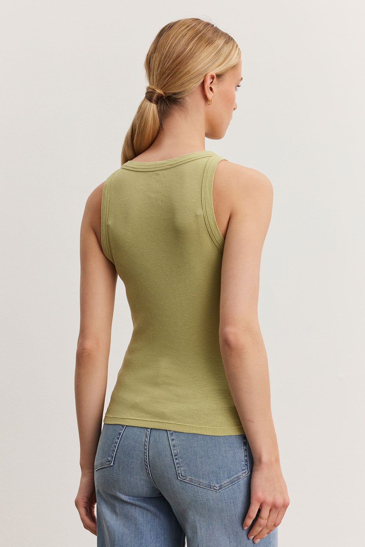   Woman with a ponytail wearing a Velvet by Graham & Spencer NOLA tank top in green and blue jeans, viewed from behind in a plain white room. 