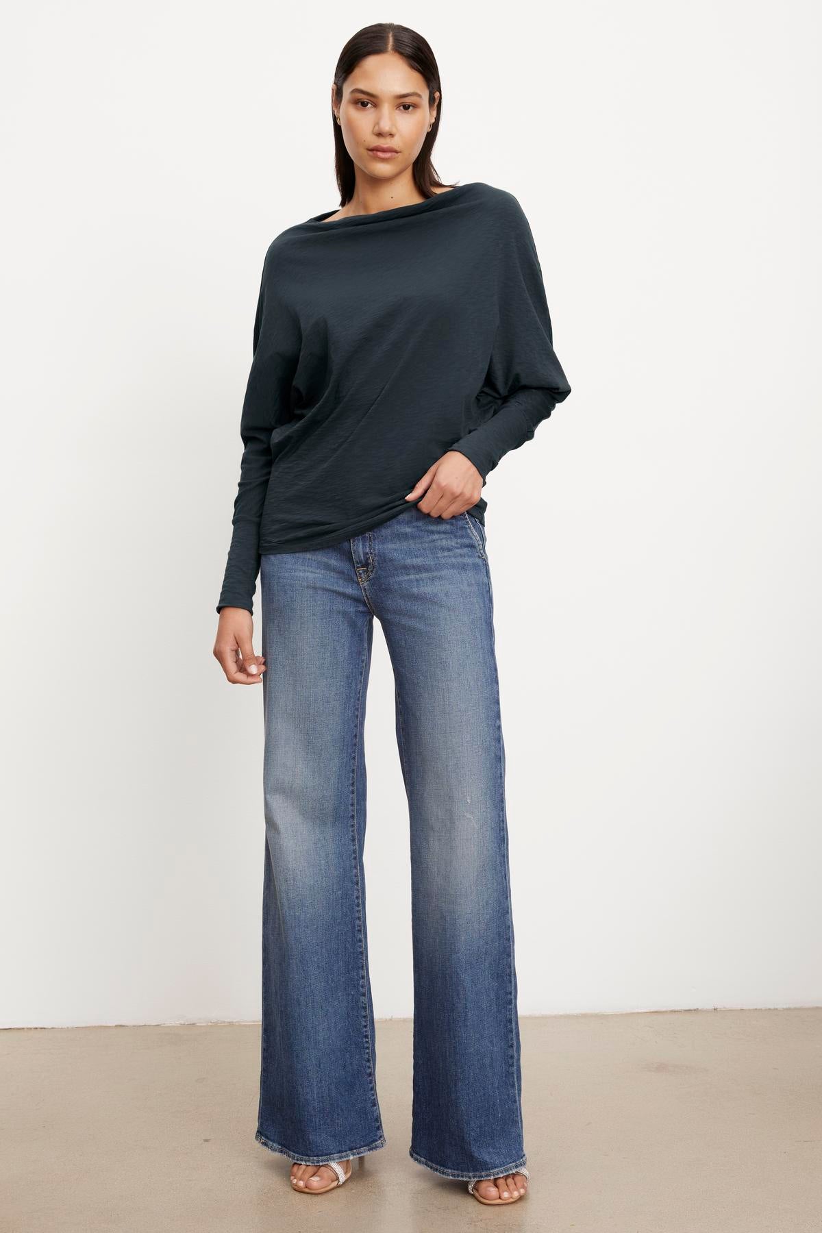   The model is wearing a Velvet by Graham & Spencer NOVALEE DOLMAN TEE with dolman sleeves and flared jeans. 