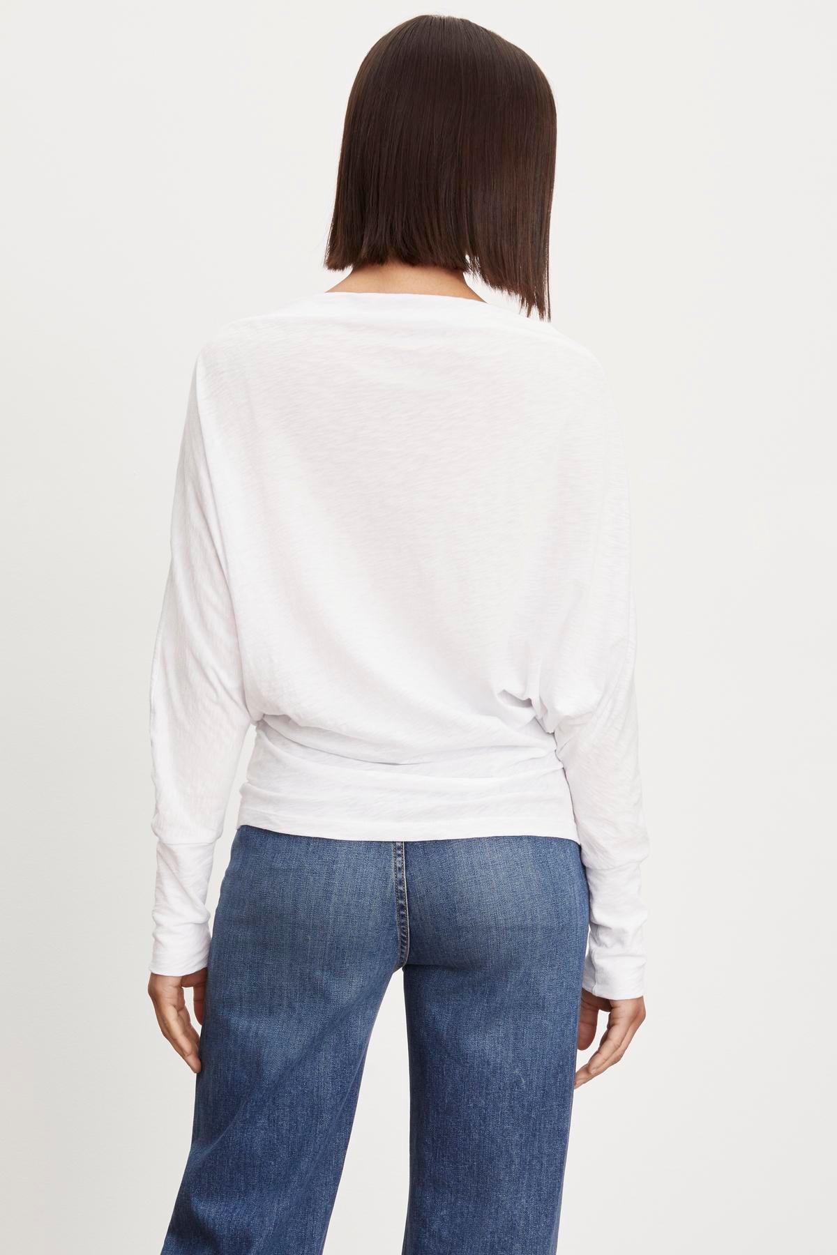   The view of a woman wearing Velvet by Graham & Spencer's NOVALEE DOLMAN TEE jeans and a white long sleeve top. 
