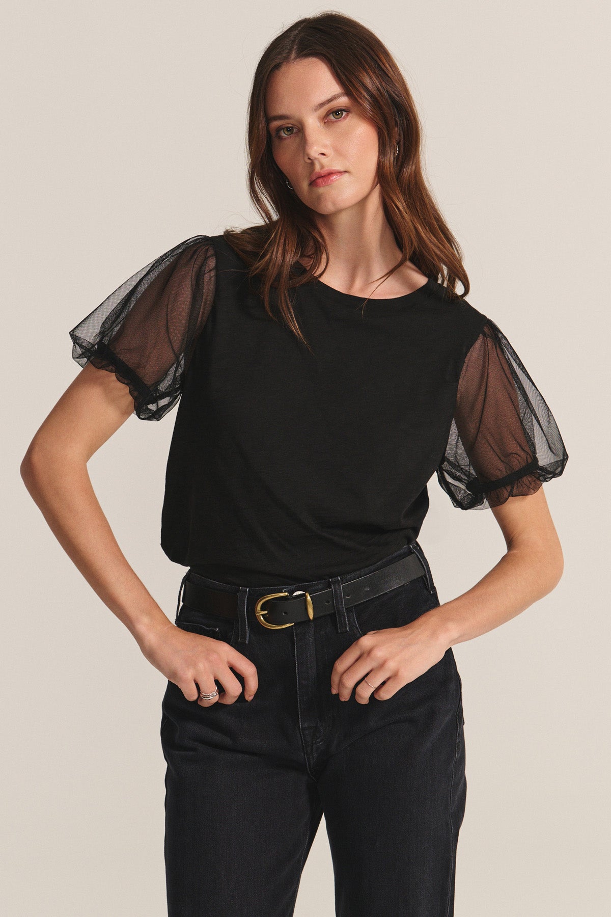 A woman wears the JUSTINE TEE by Velvet by Graham & Spencer—black cotton slub with sheer puff sleeves and a crew neck—paired with black pants, standing against a neutral background with one hand on her hip.-40263651000513