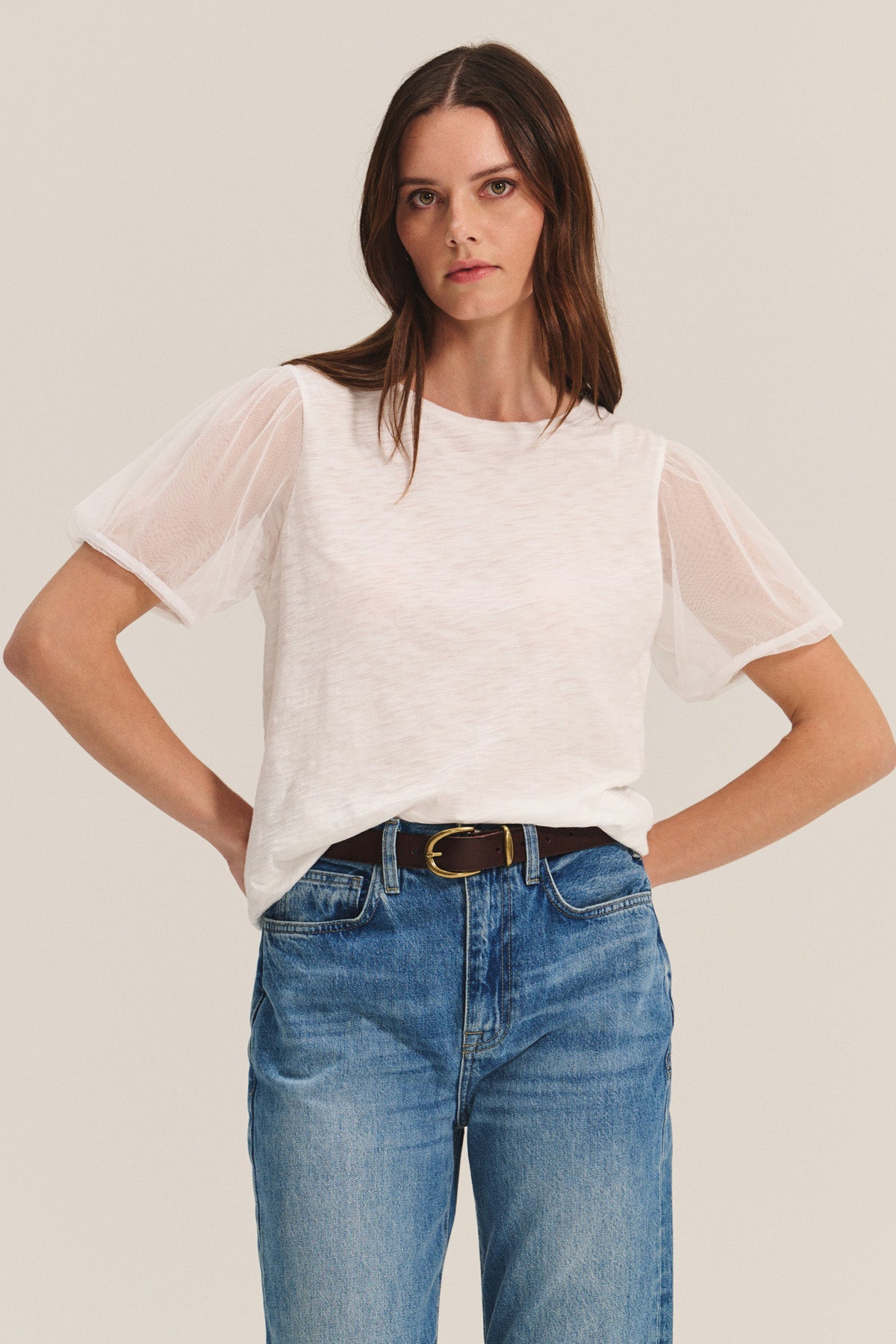 A woman wears the JUSTINE TEE by Velvet by Graham & Spencer— a cotton slub top with tulle puff sleeves and a crew neckline — paired with blue jeans and a black belt, set against a plain light background.