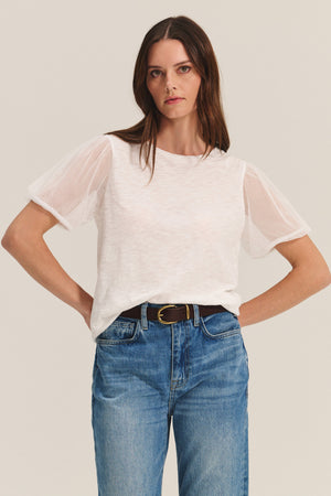 A woman wears the JUSTINE TEE by Velvet by Graham & Spencer— a cotton slub top with tulle puff sleeves and a crew neckline — paired with blue jeans and a black belt, set against a plain light background.