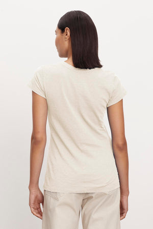 A person with straight, shoulder-length hair is facing away, wearing a light-colored Velvet by Graham & Spencer ODELIA TEE with a classic crew neckline and light-colored pants made from premium cotton against a plain background.