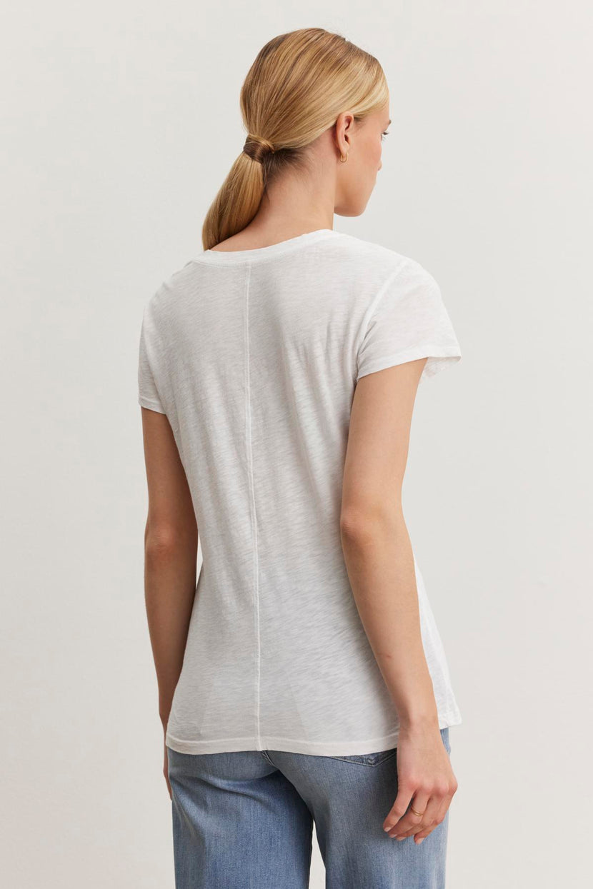 A person with blonde hair in a ponytail is facing away, wearing the Velvet by Graham & Spencer ODELIA TEE made from premium cotton slub fabric and blue jeans.