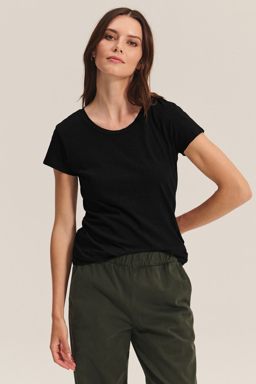A woman wearing the Velvet by Graham & Spencer ODELIA TEE—a premium cotton crewneck—paired with olive green pants stands against a neutral background.