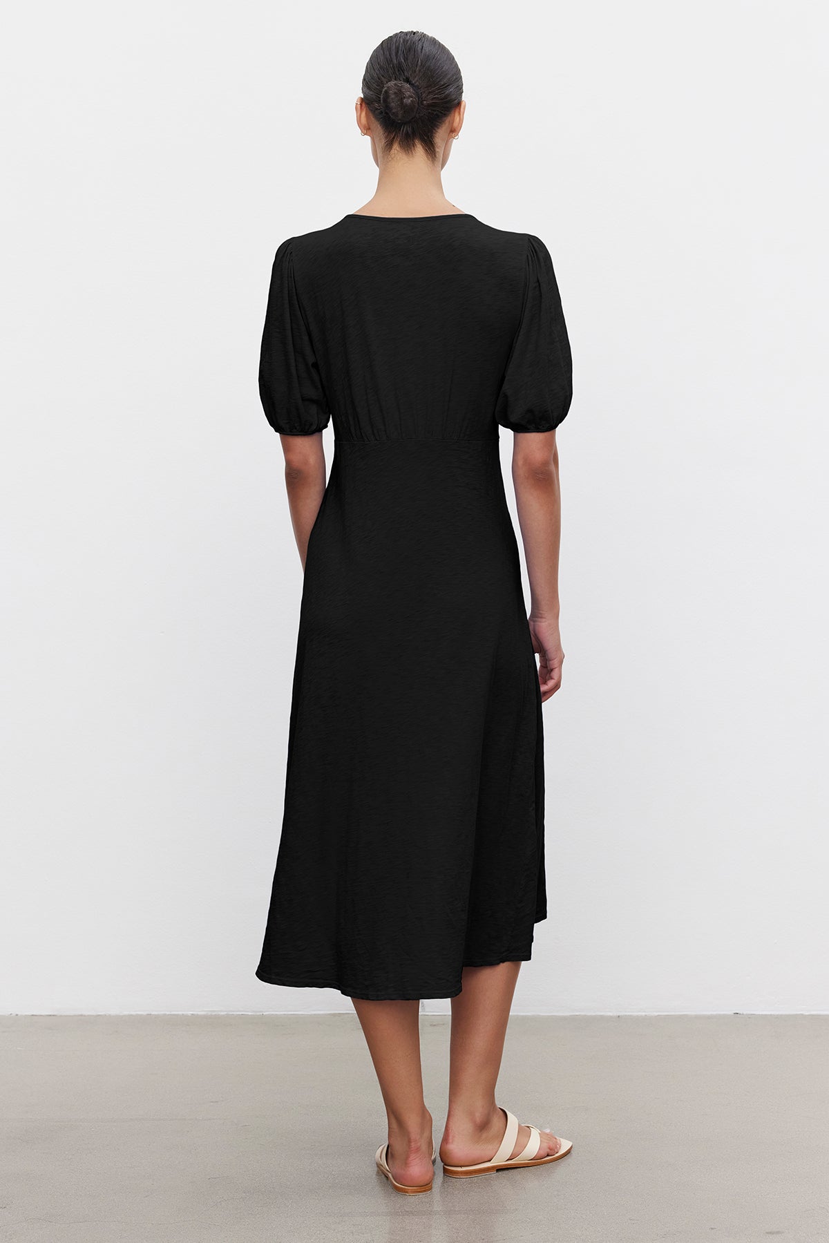   A person with hair tied up wears a Velvet by Graham & Spencer PARKER COTTON SLUB MIDI DRESS with short sleeves and sandals, standing against a plain white background. 