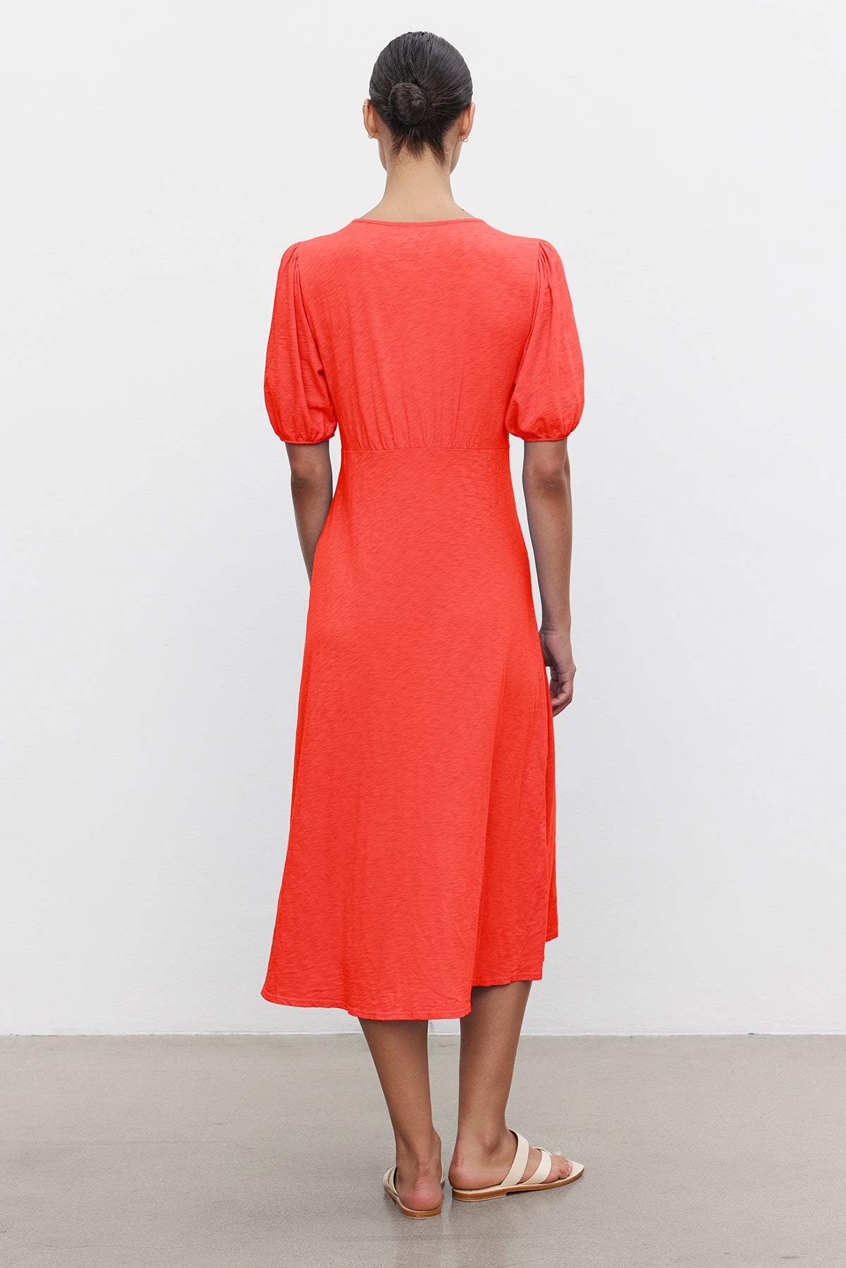 A person with hair in a bun, wearing the PARKER COTTON SLUB MIDI DRESS by Velvet by Graham & Spencer with short puffed sleeves and flat sandals, stands with their back to the camera against a plain white background.-37185421836481