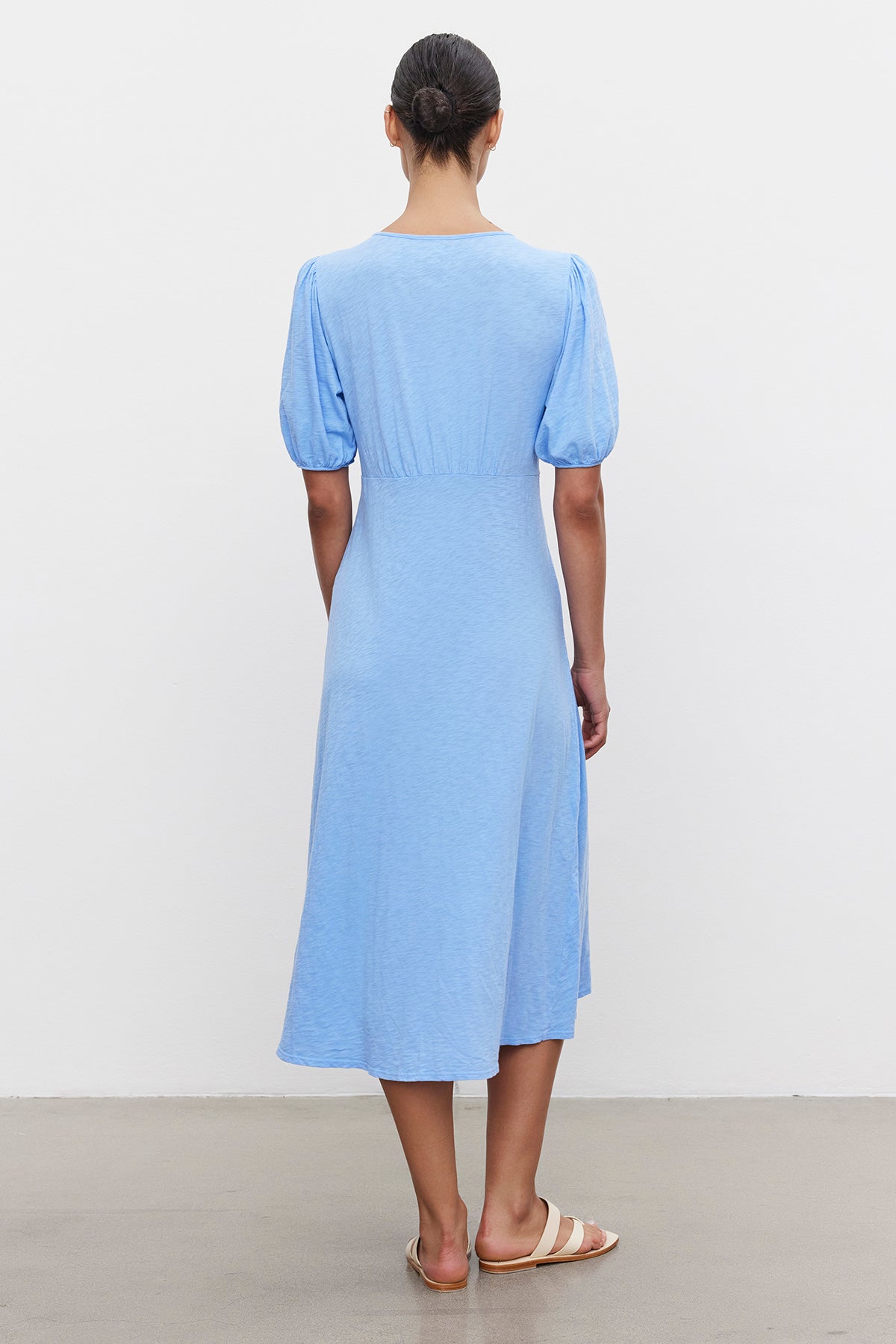 A woman stands with her back to the camera, wearing a Velvet by Graham & Spencer PARKER COTTON SLUB MIDI DRESS with puffed sleeves and sandals.-36691474809025