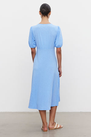 A woman stands with her back to the camera, wearing a Velvet by Graham & Spencer PARKER COTTON SLUB MIDI DRESS with puffed sleeves and sandals.