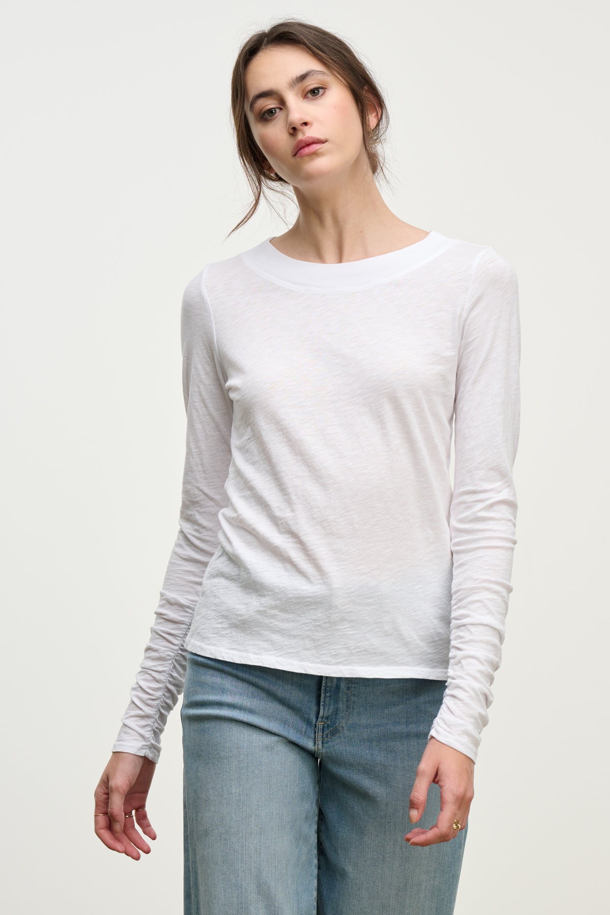 A woman wears the versatile PRIYA TEE by Velvet by Graham & Spencer—a relaxed fit, plain white long-sleeve shirt—with light blue jeans, standing against a neutral background.-39814912803009