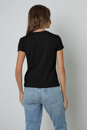 The back view of a woman wearing jeans and a black Velvet by Graham & Spencer SIERRA CREW NECK TEE.
