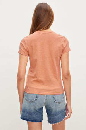 The back view of a woman wearing a Velvet by Graham & Spencer SIERRA CREW NECK TEE with a retro vibe and denim shorts.
