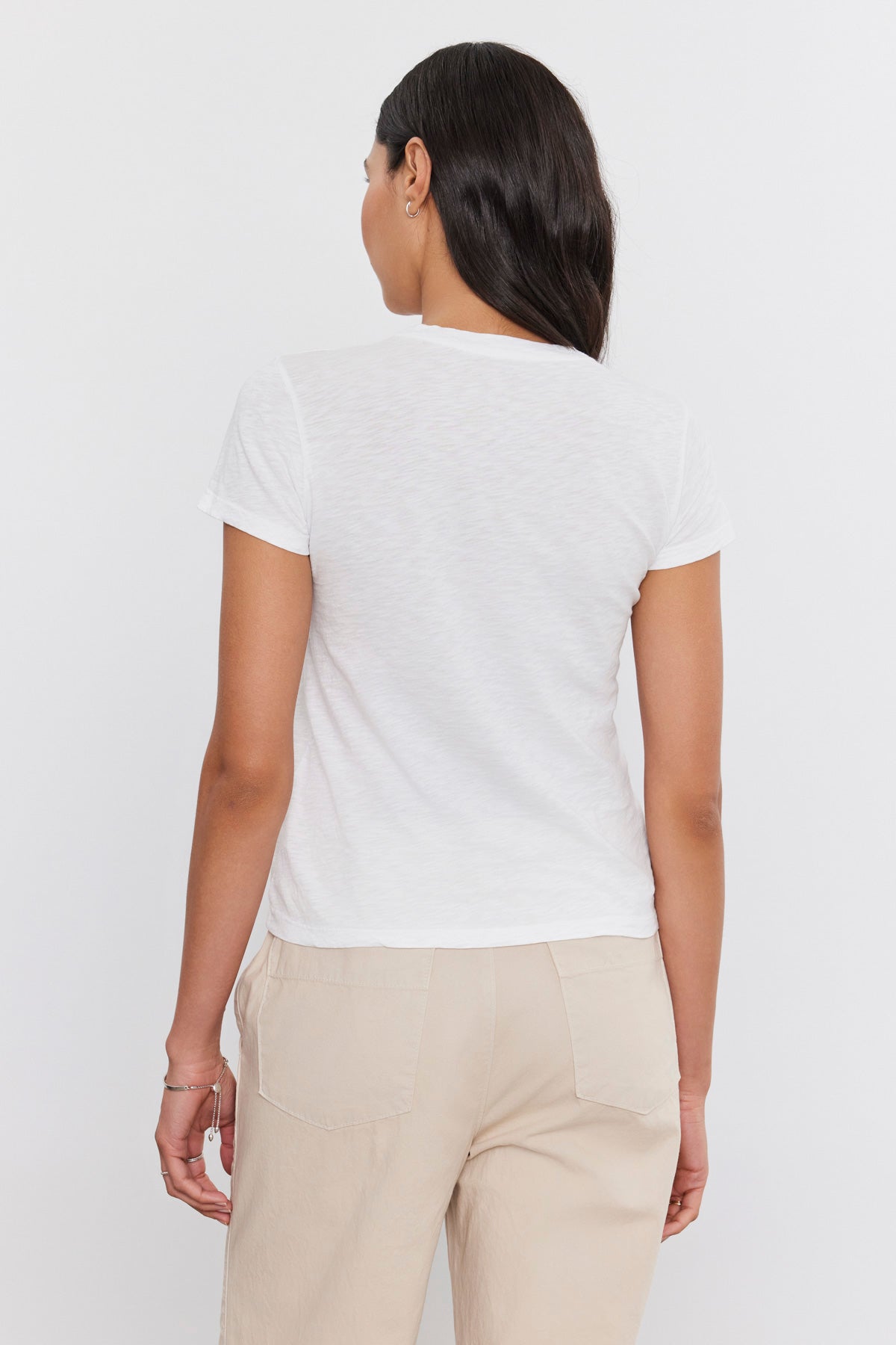   The back view of a woman rocking a retro vibe in a white cotton SIERRA CREW NECK TEE from Velvet by Graham & Spencer and tan pants. 