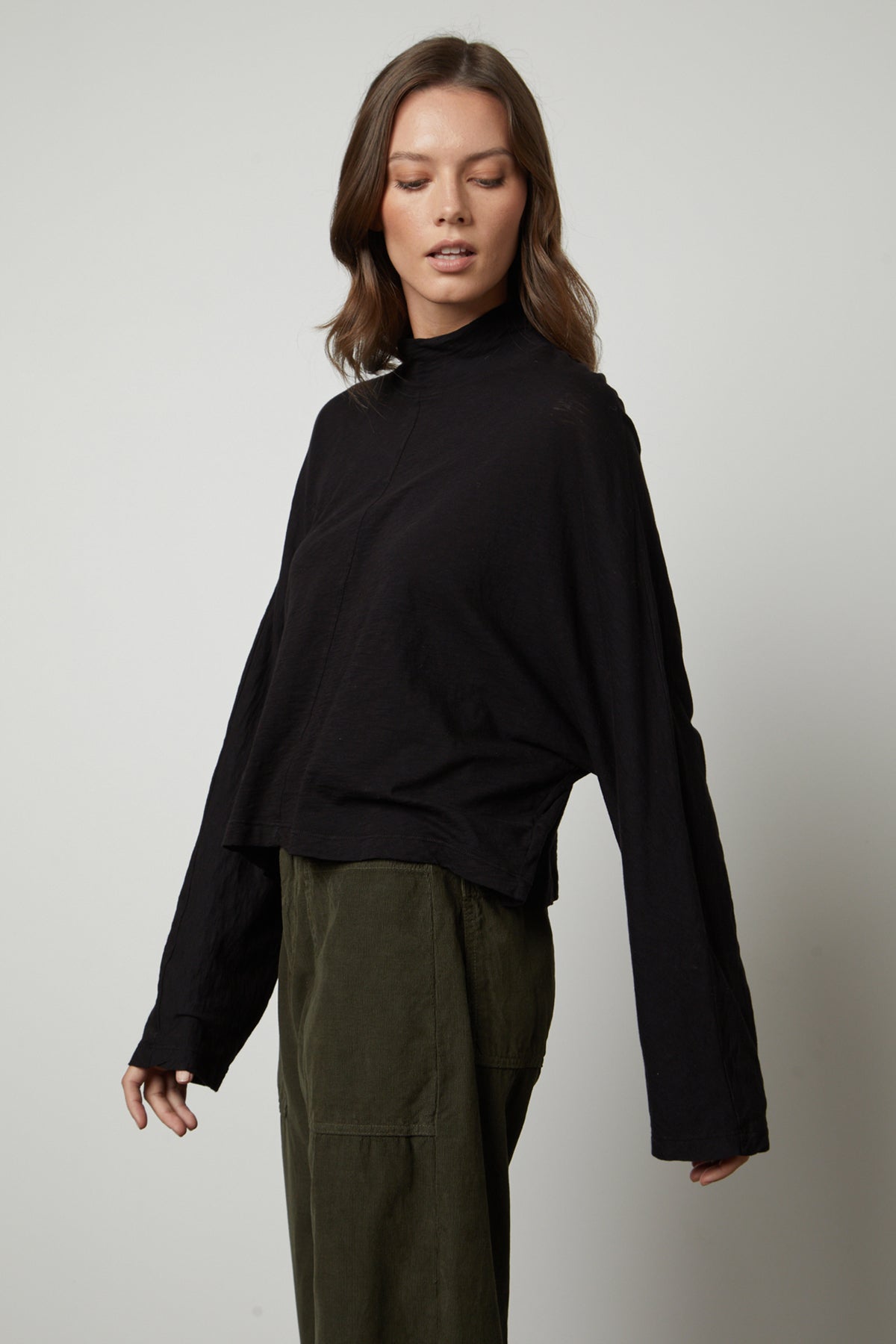The model is wearing a Velvet by Graham & Spencer STACEY MOCK NECK TEE and green trousers.-26895469347009