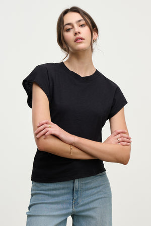 Woman wears the STERLING TEE by Velvet by Graham & Spencer, a black cotton slub t-shirt with dolman short sleeves, paired with blue jeans, standing with arms crossed against a plain light background.