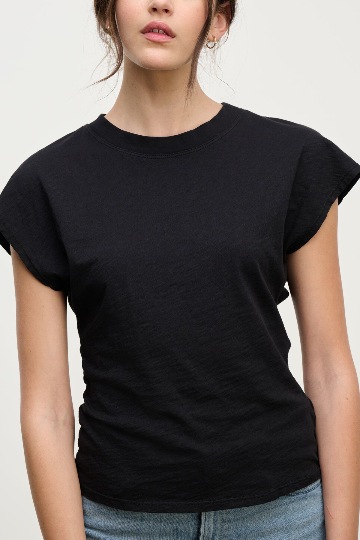 A woman wearing the STERLING TEE by Velvet by Graham & Spencer, a black cotton slub short-sleeve t-shirt, and light blue jeans stands against a plain light background.-Hover Image