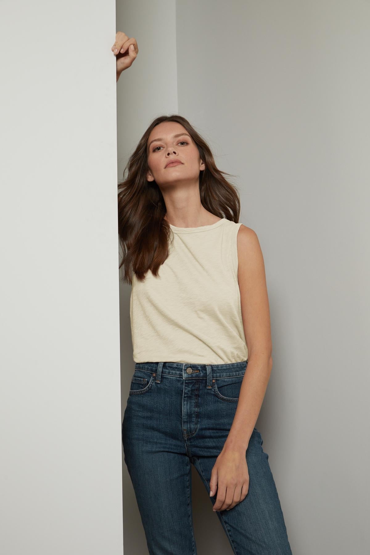   A woman in jeans and a Velvet by Graham & Spencer TAURUS COTTON SLUB TANK leaning against a wall. 