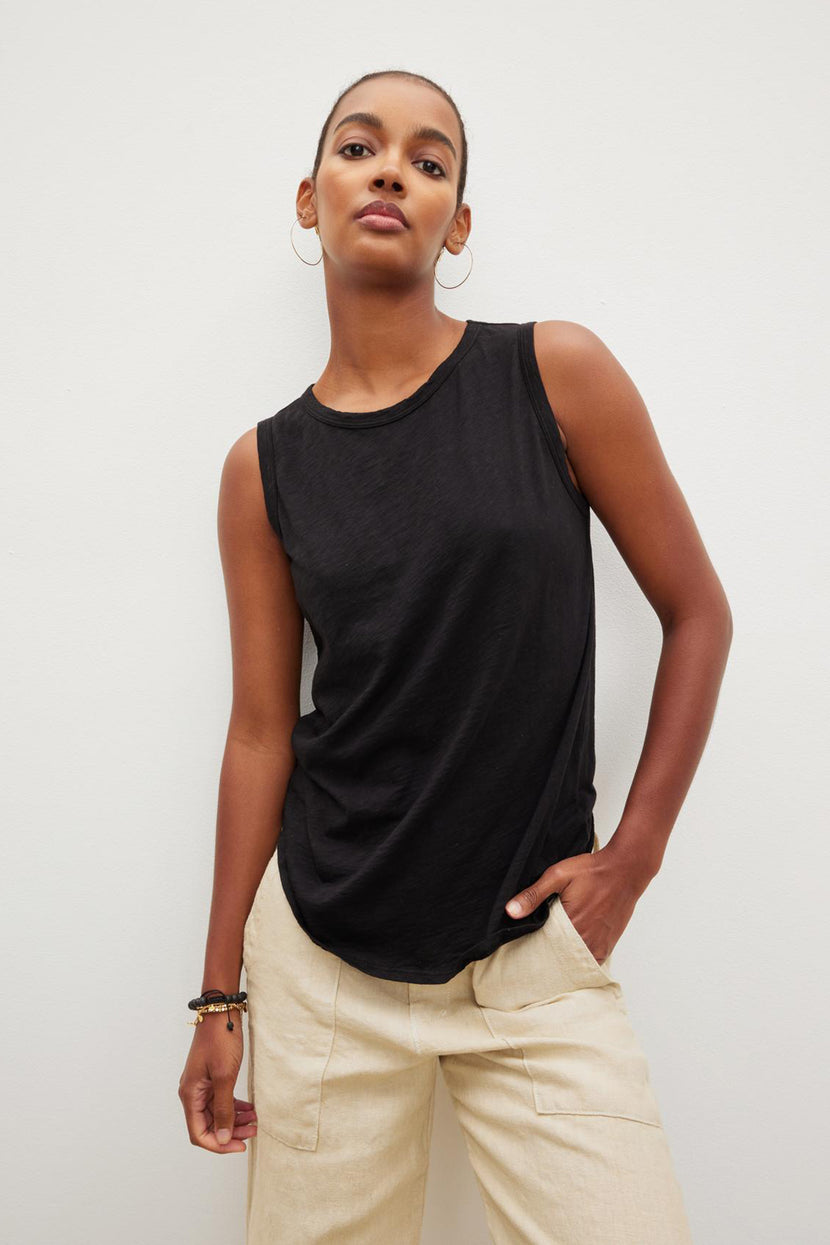 A person wearing a black Velvet by Graham & Spencer TAURUS TANK TOP and beige pants, made from textured cotton slub, stands against a plain white background with one hand in a pocket.