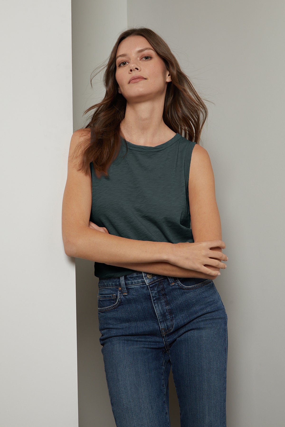   a woman in jeans and a Velvet by Graham & Spencer TAURUS COTTON SLUB TANK leaning against a wall. 