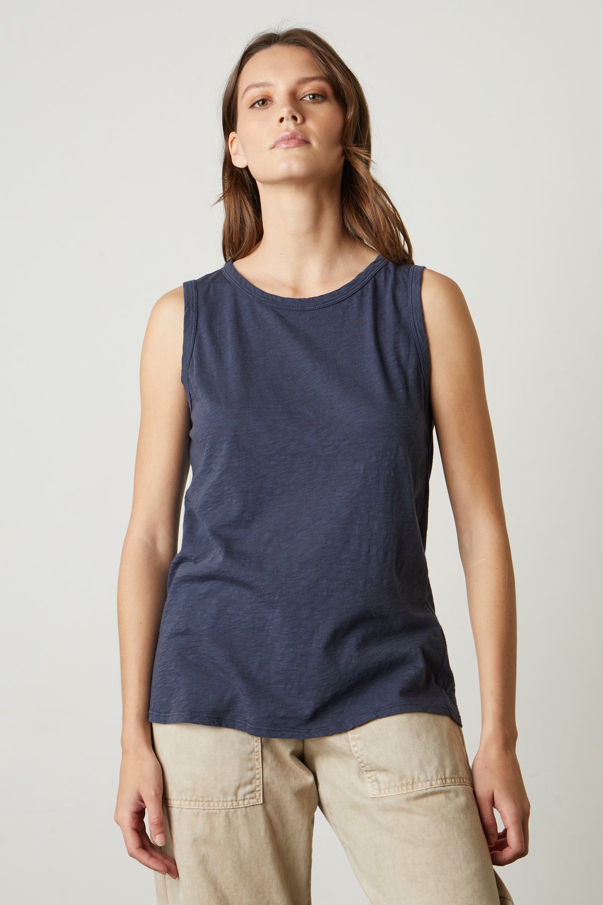   A woman wearing a Velvet by Graham & Spencer TAURUS TANK TOP and light beige pants stands against a plain background. 