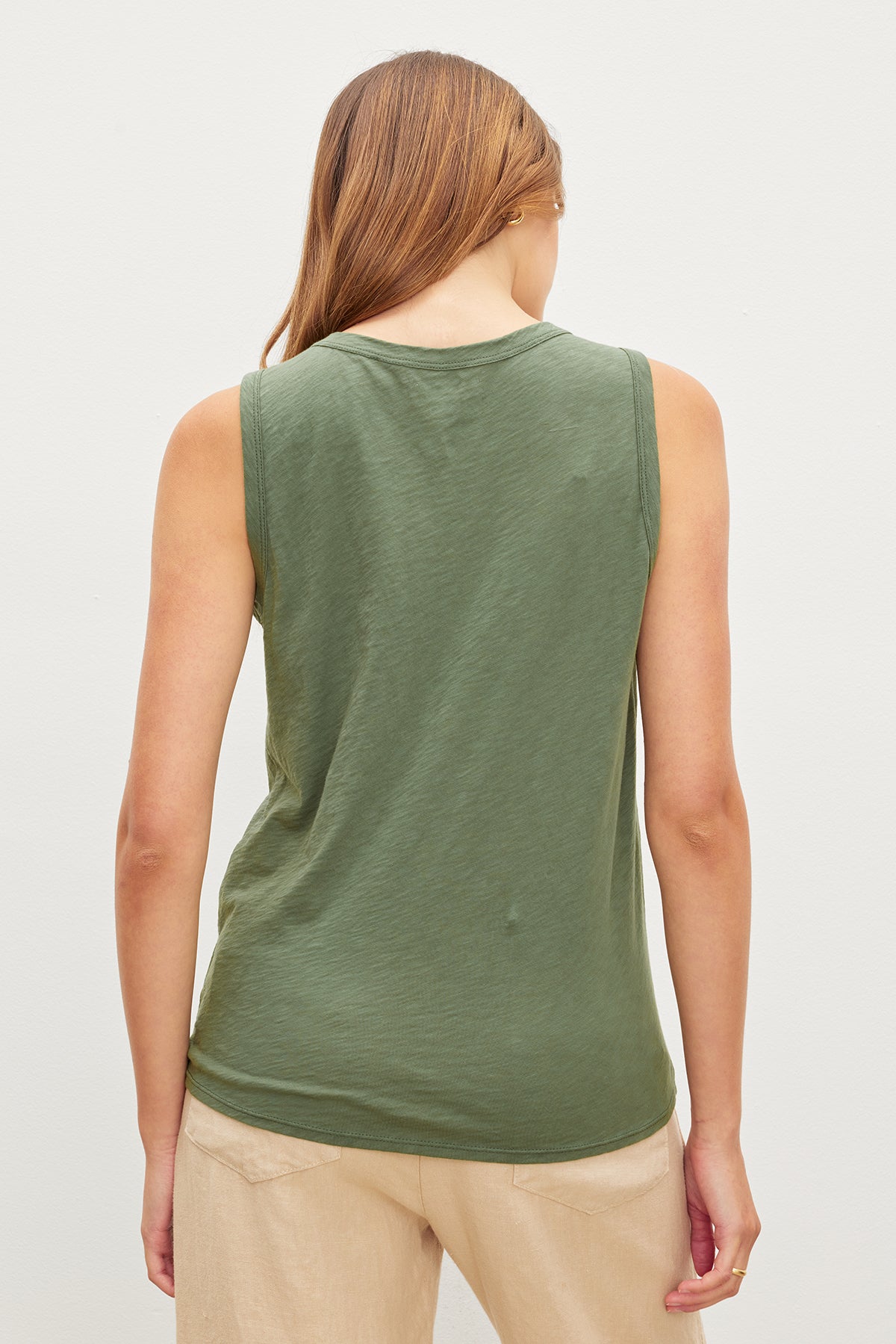 Woman viewed from behind, wearing a green crew-neck TAURUS COTTON SLUB TANK and beige pants, standing against a white background by Velvet by Graham & Spencer.-35982876410049